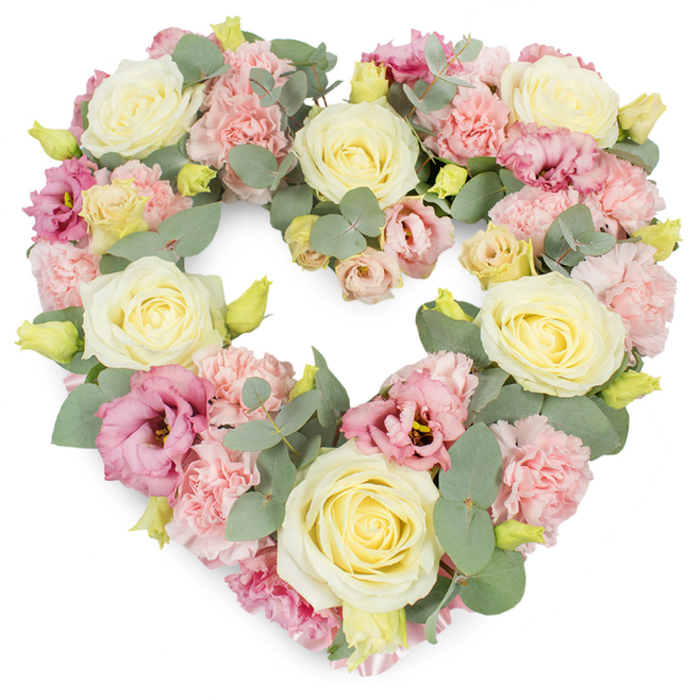 A luxurious heart-shaped tribute fills the frame, meticulously crafted from soft-toned flowers and cool greenery, set against a stark white backdrop that lets every pastel hue stand out. The heart is complete and symmetrical, with no gaps in its outline, as if the flowers themselves are gently embracing the space within. Cream and pale yellow roses form the main structure, their blooms fully formed yet still slightly cupped, each petal layered with precision to give a plush, almost satin-like texture. Nestled closely around them, ruffled light pink carnations create a delicate, feathery contrast, their edges frilled like lace, softening the composition and evoking tenderness. Richer pink and mauve lisianthus flowers are dotted throughout, some more open, some just beginning to unfurl, their petals thinner and more flowing than the roses, introducing an airy grace. Between the blossoms, stems of silvery-green eucalyptus weave gently, their round leaves adding shape, depth, and a hint of woodland calm; you can imagine the subtle, soothing scent they release when freshly arranged. Here and there, small yellow-green buds emerge, a quiet nod to renewal and the continuity of life even in moments of goodbye. The whole design feels serene and composed, making it an ideal wreath for a funeral, committal, or memorial service in Old Malden or nearby New Malden, perhaps placed beside a framed photograph or candles. Created with the care of an experienced local florist, this heart wreath conveys affection, respect, and an enduring connection, offering comfort to family and friends gathered to remember someone cherished.